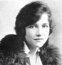 A white woman with light eyes and dark hair, wearing a fur wrap