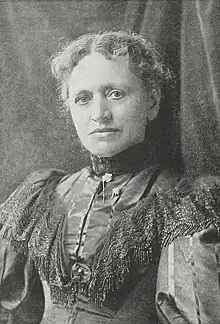 19th-century B&W portrait photo of an old woman with her hair in an up-do, wearing a dark, ruffled blouse.