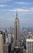 Aerial view of a 100-story building with several setbacks; the building tapers into a large circular spire near its 90th floor and is topped by a large antenna.