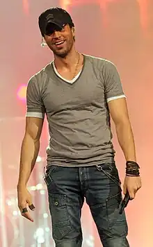 A man wearing a short-sleeve short and cap smiles while holding a microphone.