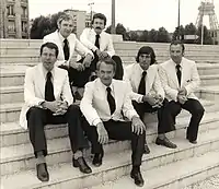 Six men in suits sitting on steps.