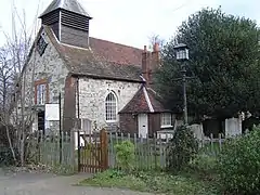 The western part of a simple stone church with a tiled roof and a weatherboarded bellcote