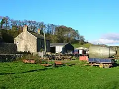 A green field with farm buildings and farm equipment, with a small hill behind