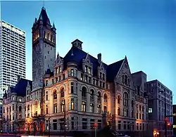 A Romanesque style building on a street corner. Photographed at dusk so the sky is still blue but the inside lights and street lights are on.