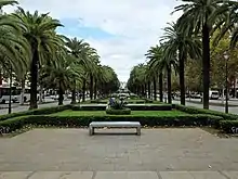 A pedestrian area with benches surrounded by trees between two roadways