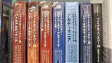 Seven thick large paperback books, each with different Japanese writing on the binding, wrapped in plastic, sitting on a shelf in a row