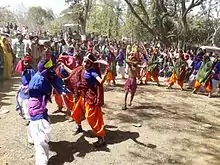 Colourfully-dressed dancers and a young boy with a bow and arrow