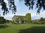 a stone building covered in greenery, with grass in the foreground