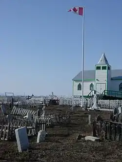 The wooden church and a maple leaf flag on a flagpole at Fort McPherson