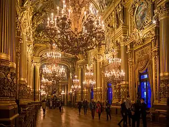 Grand foyer of the Palais Garnier, inspired by the Hall of Mirrors of the Palace of Versailles, but with some ornaments taken from other historical styles, like the neo-Renaissance column lower parts, or the Greek Revival lyres at the tops of windows, by Charles Garnier, 1860–1875