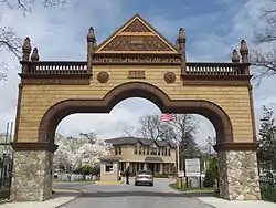 A road with an arch around it. The arch has a stone base and a tan brick with brown outline top of the arch that starts about 5 feet above the ground. At the very top of the arch it reads "1848 Cypress Hill Cemetery 833" with 833 being the street number.