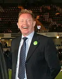 A laughing Caucasian man in a black suit with short blonde hair.