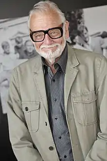 an older man with black glasses smiles at the camera.