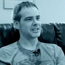 Grant Kirkhope sitting at a couch.  This photo is a close-up of his face, showing him in the middle of a conversation.