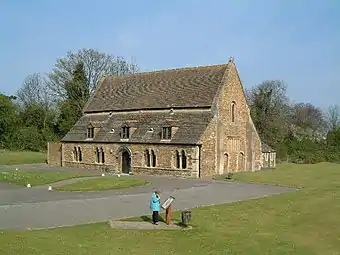 A tidy building like a large barn, of red brick with long sloping roofs, dormer windows and a low arched doorway.