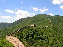 A high defensive wall with watch towers running through a mountain landscape.