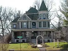 A white house with green roof. It is set back from a lawn and surrounded by bare trees