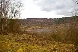 An open quarry pit in the middle of rolling, shrub covered hills