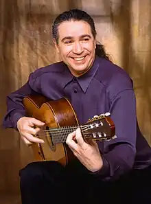 Laucke, seated in half profile, playing his guitar and smiling while looking away from the camera