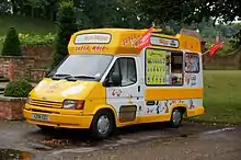  Yellow-and-white van decorated with pictures of Mickey Mouse and illustrations of the types of ice cream it sells; text on the van reads "Super Whippy" while packets of crisps and cans of fizzy drinks are visible in the window