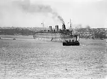 Black and white photo of a large passenger ship in an enclosed harbour. A smaller ship is visible in front of the passenger ship.