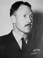 Portrait of moustachioed man in dark military uniform with pilot's wings on left pocket