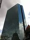 Angled, ground-level view of a broad, 60-story building with a blue-tinted, all-glass facade