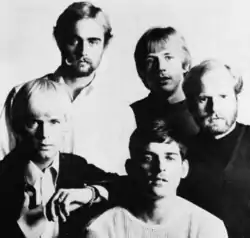 A group of five young men, two with blond hair and beards, two with blond hair and no beard, and one with dark hair and no beard