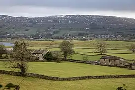 Green fields in the foreground with a mountain range in the background scattered with snow