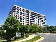 Box mid-rise grey office building behind a curving drive, beside which a metal sign reads, "Hilton, Logan Hovells, Adobe. Park Place, I and II. 7926 & 7930 Jones Branch Drive."