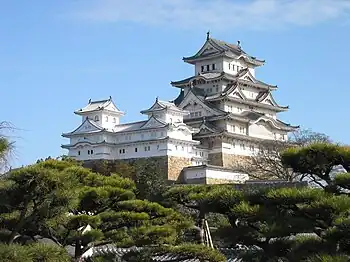 A multistoried white castle donjon with several small towers and a main tower on a platform of stone.