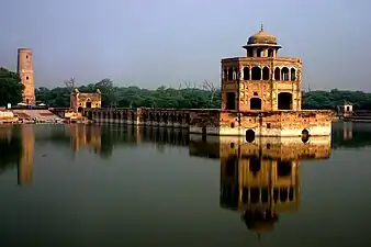 A pavilion and a wall above a pond, a large tower on the left