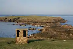 In the foreground is a building from the former RAF Skaw  and in the background is the Holm of Skaw, with its lighthouse. At low tide it seems that it should be possible to walk out to the holm, but a deep channel runs between the rocks.