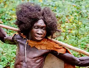 A smiling young boy with dark skim in loose clothing holding a spear