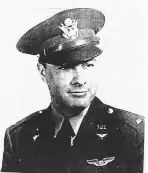 Head and shoulders of a man wearing a peaked cap and a military jacket with a winged pin on the left breast and pins on the lapels.