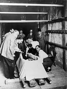 A man reaching into an open coffin as several others watch