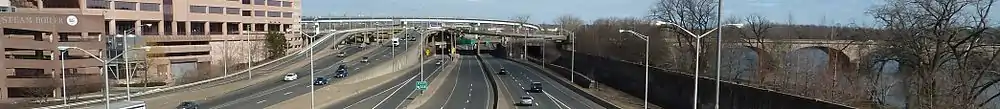 A highway interchange with 6 roads visible with several cars on the road. A building is on the left side of the interchange.