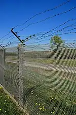 Expanded metal fence against a blue sky with rows of barbed wire lining the top