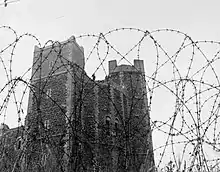 Tower with a soldier stood on top and barbed wire in front.