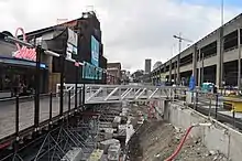 An open trench with a temporary steel bridge separates a boardwalk business from a parking lot.