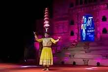 A costumed woman balancing pots on her head on stage