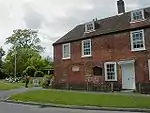 Photograph of a two-story brick house with dormer windows emerging from the roof to suggest a small third story.