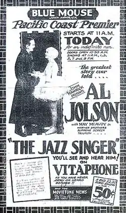 Advertisement from the Blue Mouse Theater announcing the Pacific Coast premiere of The Jazz Singer, billed as "The greatest story ever told". A photo of stars Al Jolson and May McAvoy accompanies extensive promotional text, including the catchphrase "You'll see and hear him on Vitaphone as you've never seen or heard before". At the bottom is an announcement of an accompanying newsreel.