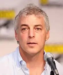 A headshot of a gray-haired man, opening his mouth to speak