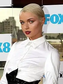 A bust photo of a young white woman, wearing a white blouse; she has blonde hair, and is facing the camera.