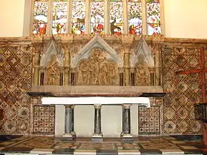 A marble reredos beneath a stained glass window, with three scenes from the Crucifixion; a granite altar with six pillars