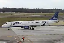 A white plane with the words "jetBlue" painted on the front and a blue tailfin taxies at an airport