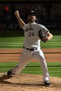 A man in a white baseball uniform preparing to pitch the ball from the mound