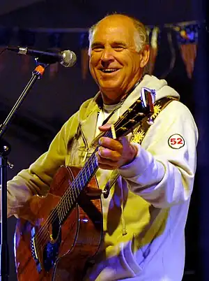 A balding man singing into a microphone and playing a guitar