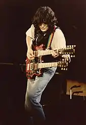 A colour photograph of Jimmy Page performing on stage with a double-necked guitar